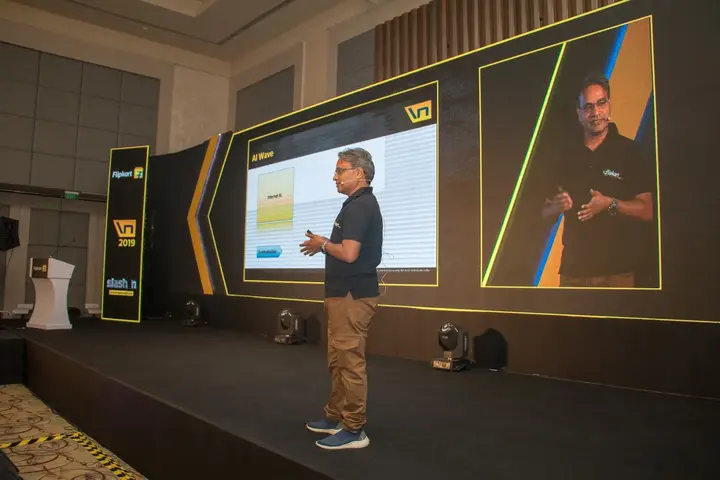Speaker presenting on a stage framed by angular LED panels