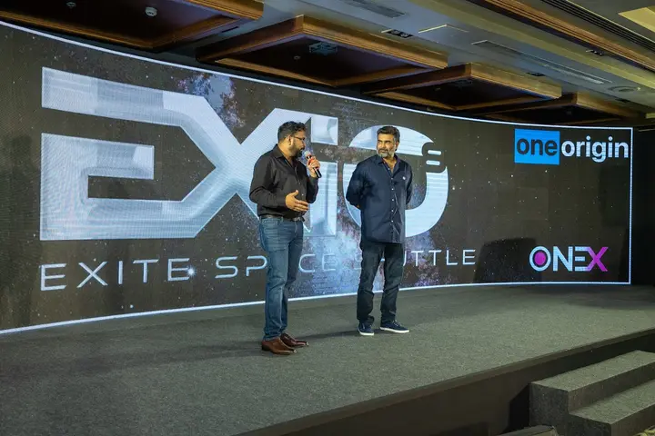 Two presenters on stage at the OneOrigin EXITE event