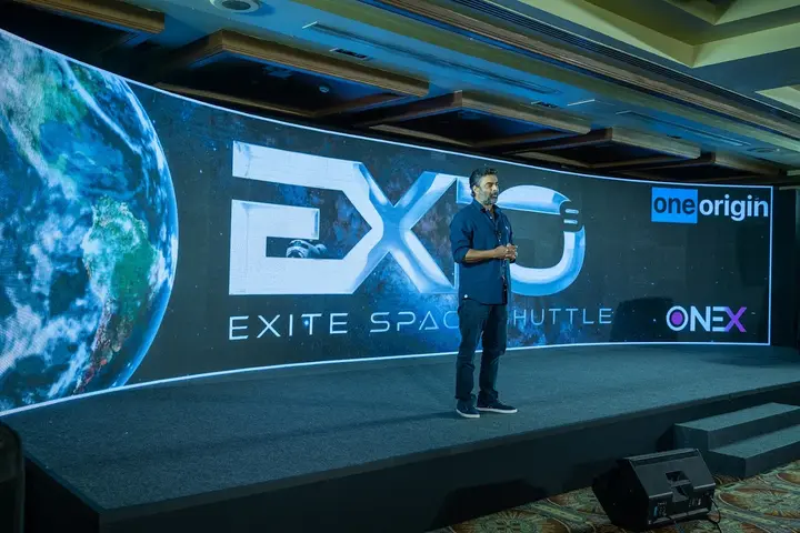 Presenter on stage with an Earth graphic on the LED wall at the OneOrigin EXITE event